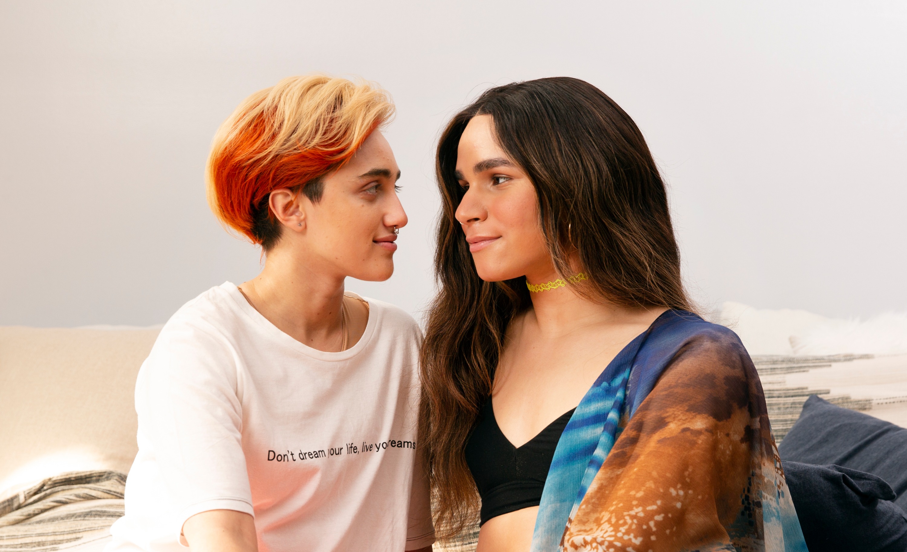 A transmasculine gender-nonconforming person and transfeminine non-binary person looking in each others eyes
